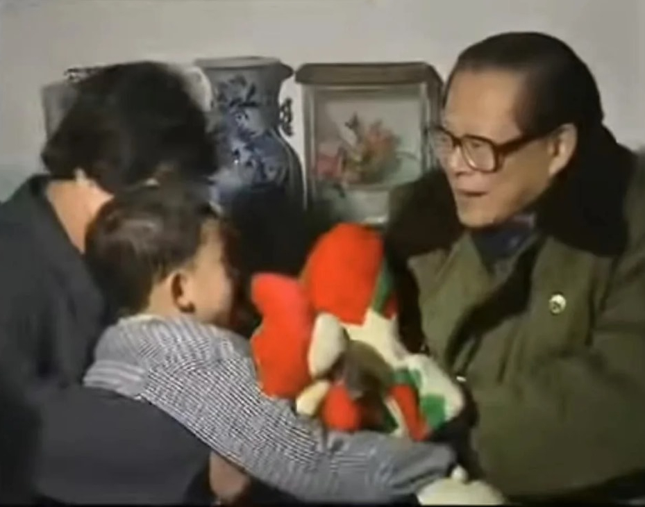 農戶懷中的小孩接過江澤民贈送的公雞玩偶。網上圖片