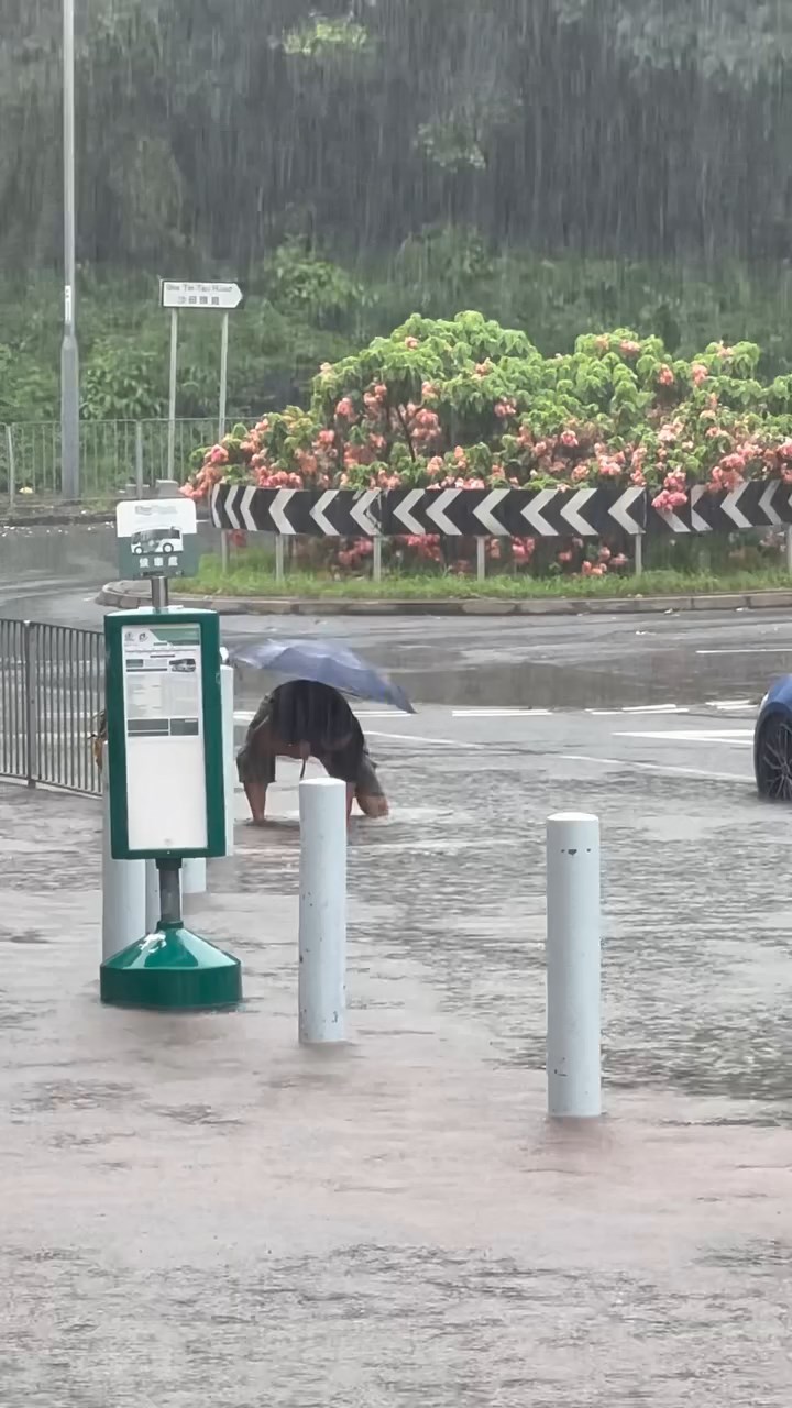 一名中年男子冒着大雨伸手落積水清走垃圾。threads@_.yuching