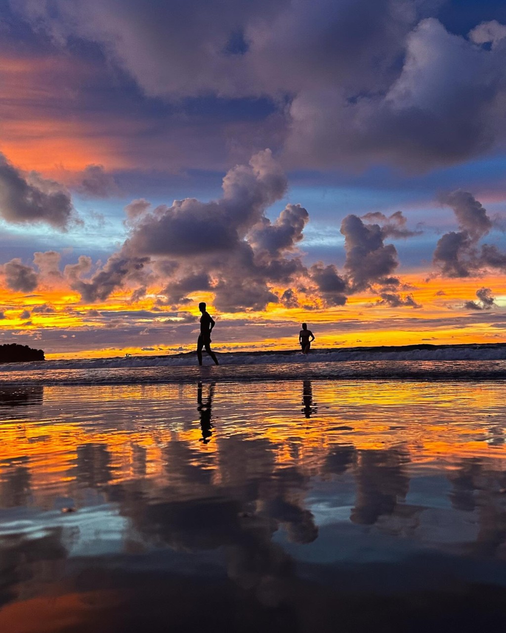 穿着泳装的二人在夕阳下漫步沙滩，相当浪漫。