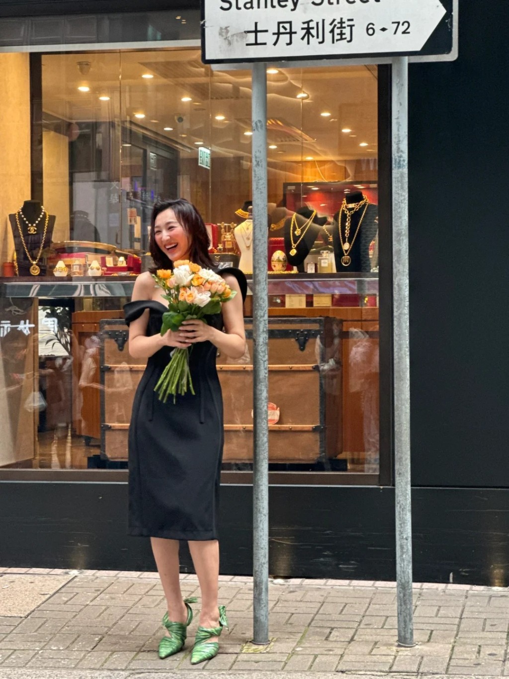 照片见高海宁身穿黑色连身裙，手拿着一束鲜花，笑得非常灿烂。