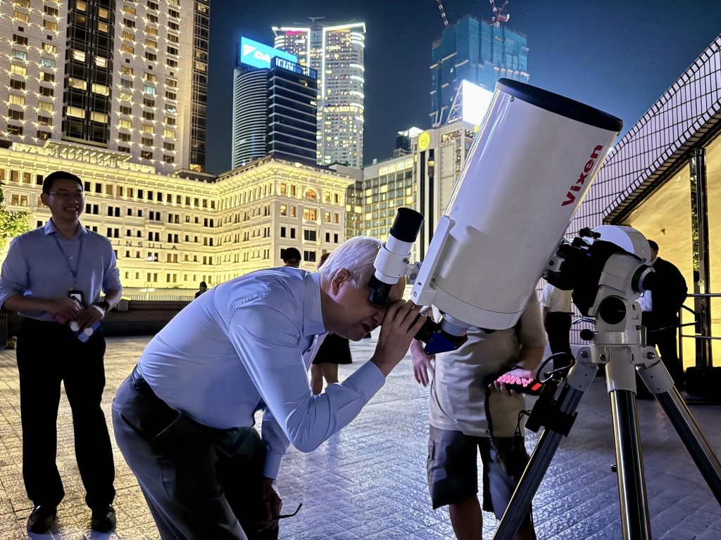 謝展寰夜幕下和市民在天台透過天文望遠鏡觀賞維港上的星光，一起體驗夜繽紛的香港。（環境及生態局FB圖片）