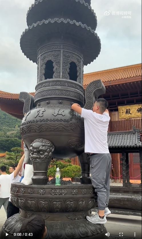 深圳弘法寺有游客爬上大香炉捡拿其他游客扔进去的香油钱。