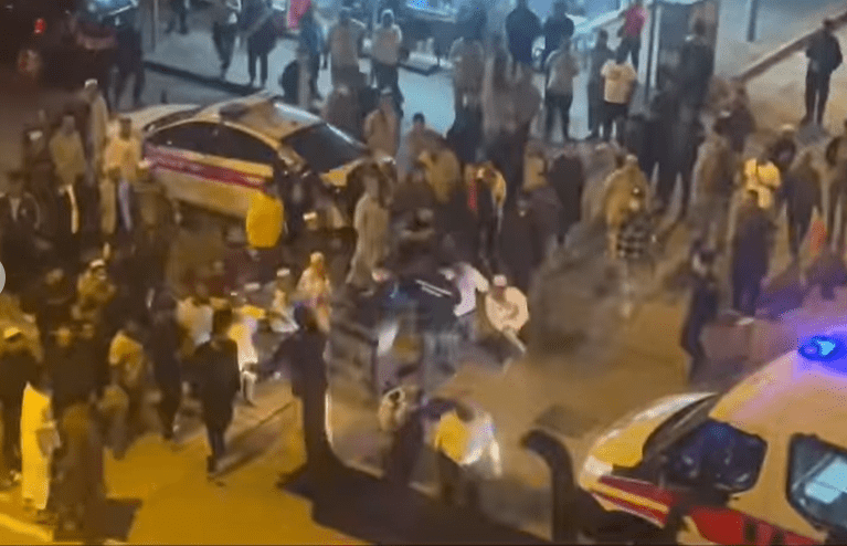 警員將一名白衫男子帶上警車。後面有人欲追趕。fb香港突發事故報料區
