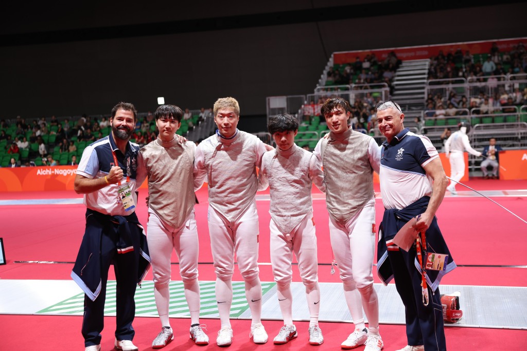 世界第二的香港男花隊在兩位教練Greg(左一)及Maurizio(右一)的帶領下,輕鬆取得首圈勝利,右二起:蔡俊彥、何承謙、張家朗及梁千雨,何承謙及梁千雨都是第一次參加亞運會,他們在首圈對印度都有落場比賽。徐嘉華攝 世界第二的香港男花隊在兩位教練Greg(左一)及Maurizio(右一)的帶領下,輕鬆取得首圈勝利,右二起:蔡俊彥、何承謙、張家朗及梁千雨,何承謙及梁千雨都是第一次參加亞運會,他們在首圈對印度都有落場比賽。徐嘉華攝