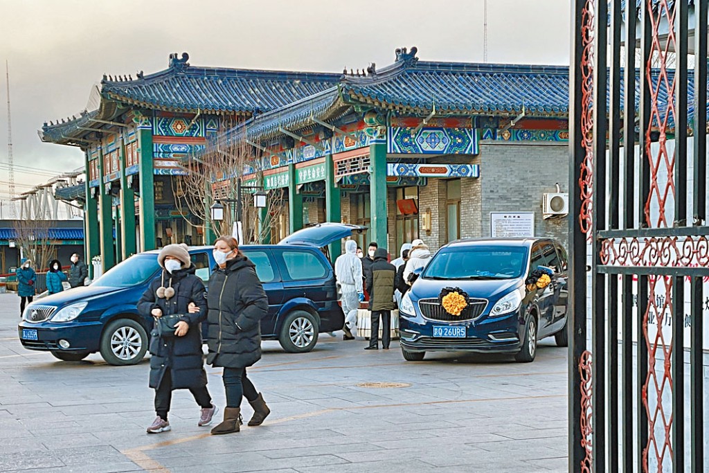 北京一家殯儀館外,穿着防護服的工人在舁送遺體。