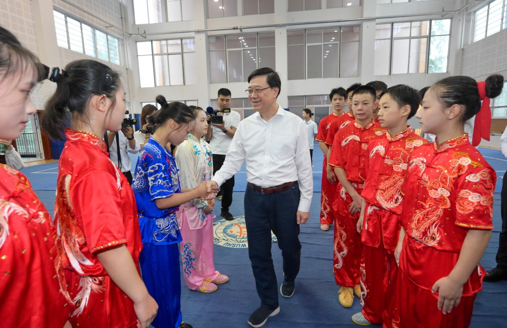 李家超（中）到訪四川香港馬會奧林匹克運動學校，與武術學生握手。
