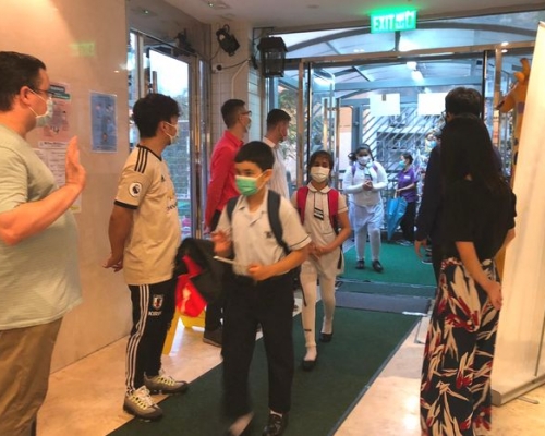 有学校教师在校门处走廊列队欢迎学生返校，与学生打招呼。