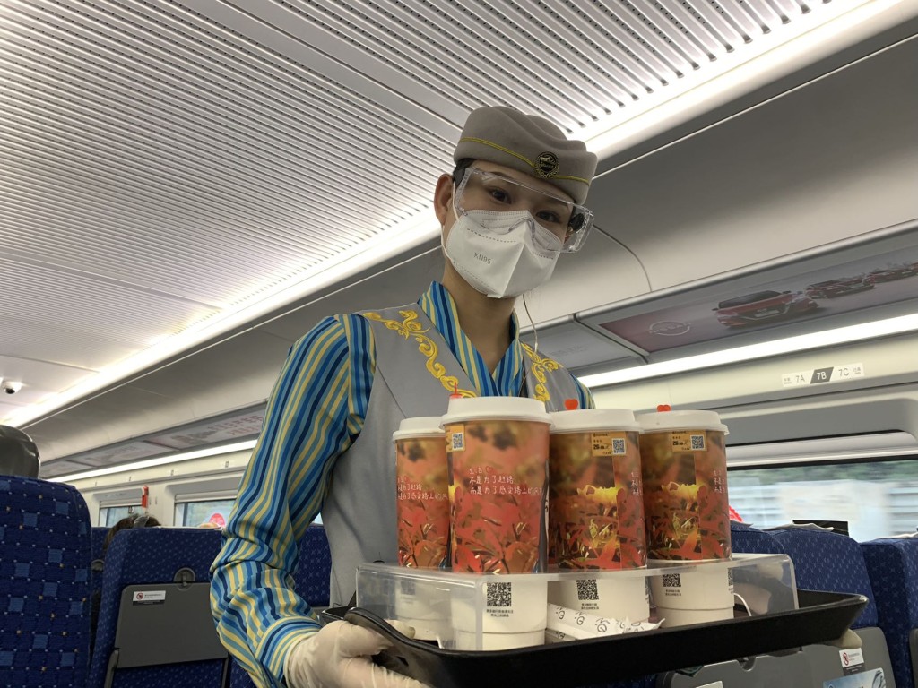 往广州东列车上，有戴上口罩和护目镜的乘务员售卖饮品。（常彧璠摄）
