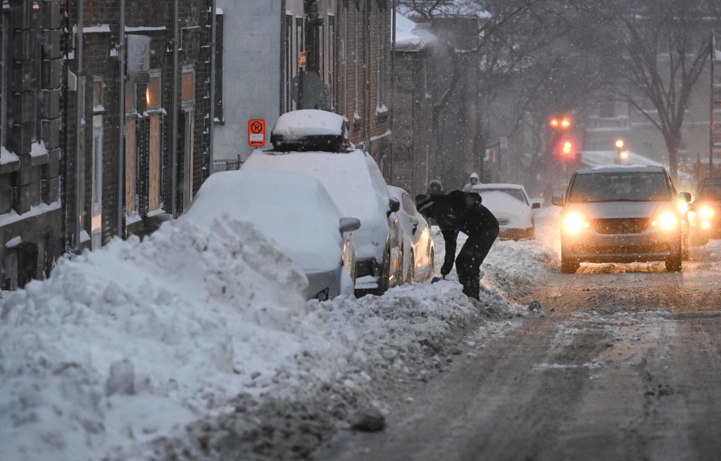 暴風雪襲擊加拿大東部，一名男子鏟雪解救被冰封汽車。AP