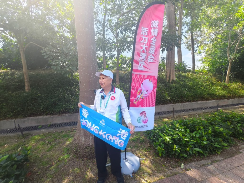 82歲的陳延邦在跨境公路自行車賽道附近做場外助理，為香港選手打氣。