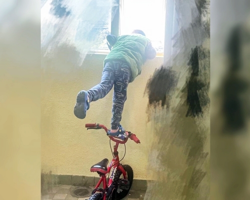 男童踩在單車上，半身探出窗外張望，情況非常驚險。「生仔要考牌系列」Facebook圖片