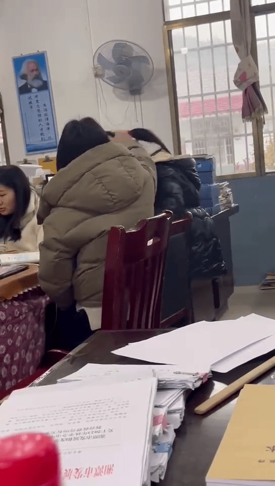 女老师拉扯女学生的马尾狂摇，近乎将学生头部撞向桌面，画面令人不适。