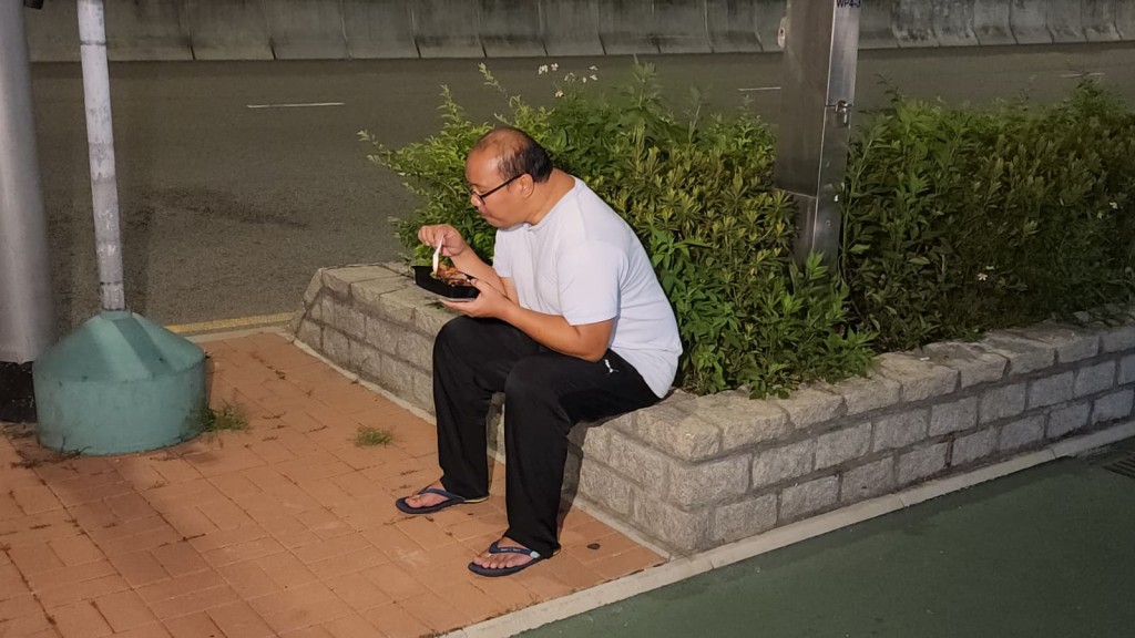 曾男手持入境處提供的飯盒，離開總部後即場開餐。黎志偉攝