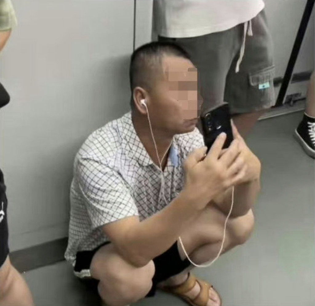 涉事大叔在地鐵裏蹲着舉起手機。
