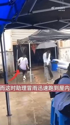 杨幂撑住雨伞，而助手就冒雨快跑。