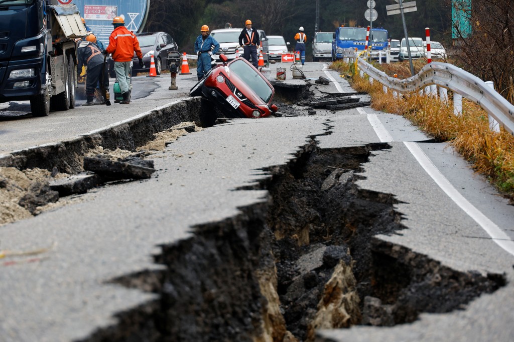日本穴水附近，地震后，工人们正在修复一辆被困在破损道路上的汽车旁的道路。路透社