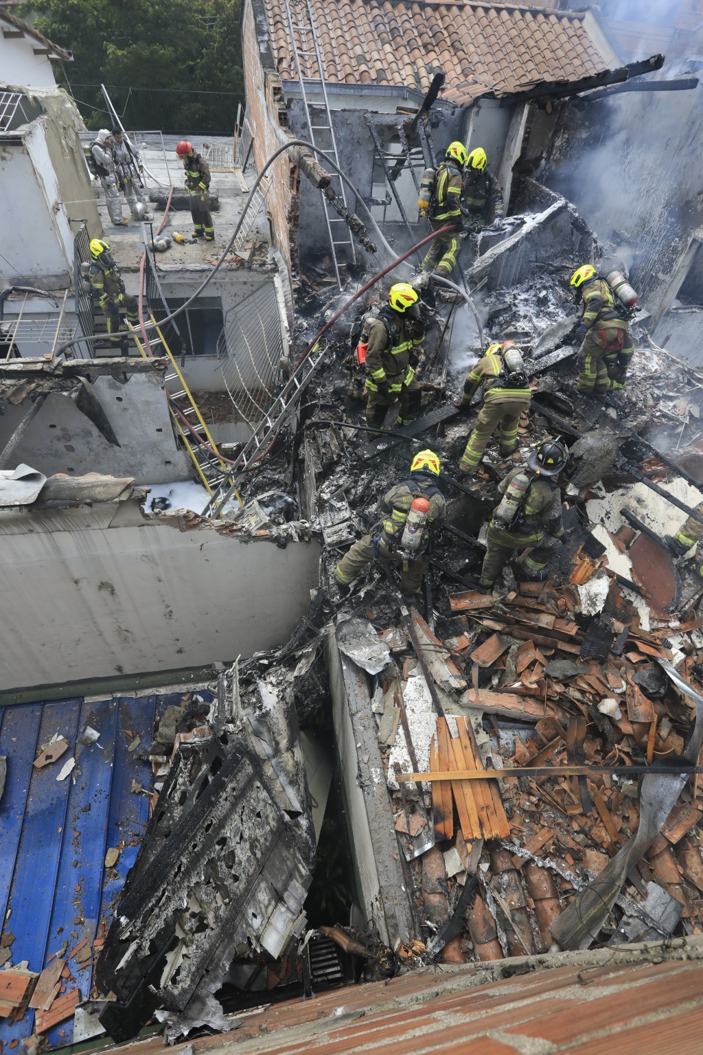 小型飞机坠毁在哥伦比亚麦德林住宅区一处屋顶，消防员在坠机现场工作。AP