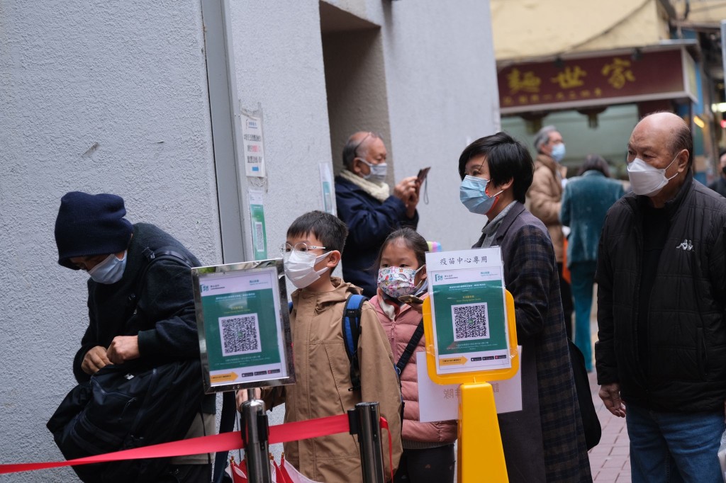 市民帶同小朋友在雨中排隊接種疫苗。