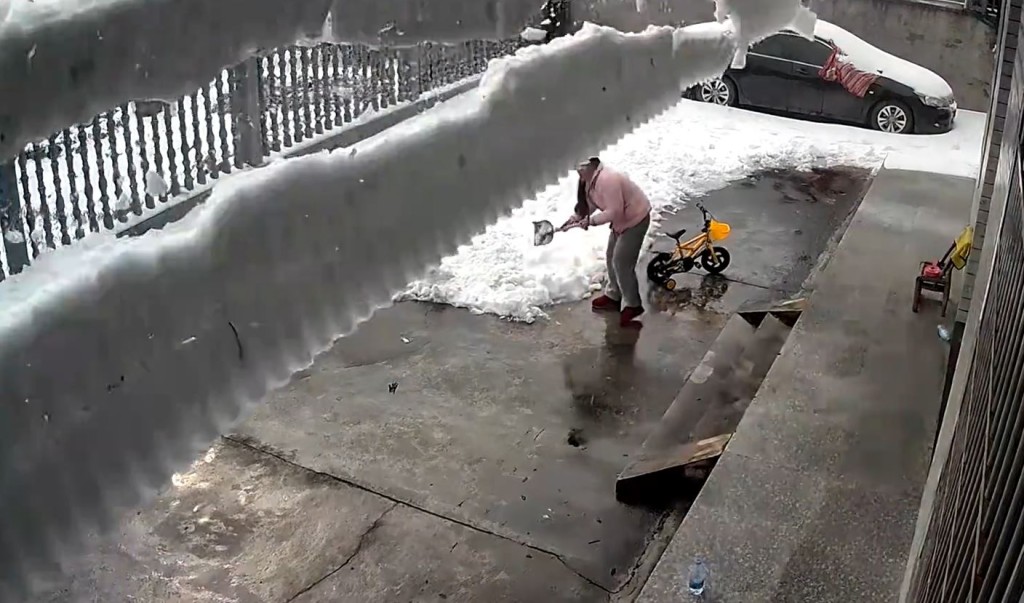 有居民清理庭院時，被屋頂的「雪瀑布」掩理。影片截圖
