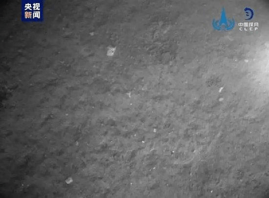 由嫦娥六号降落相机在著陆器安全著陆后拍摄，图像显示著陆器底部相对平坦，分布有少量亮色石块。 央视截图