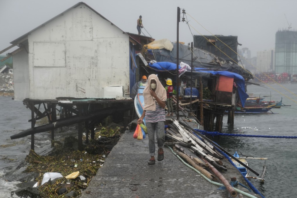 菲律賓馬尼拉，一名男子提著食物袋，另一名男子在加固屋頂，準備迎接颱風奧鹿。AP