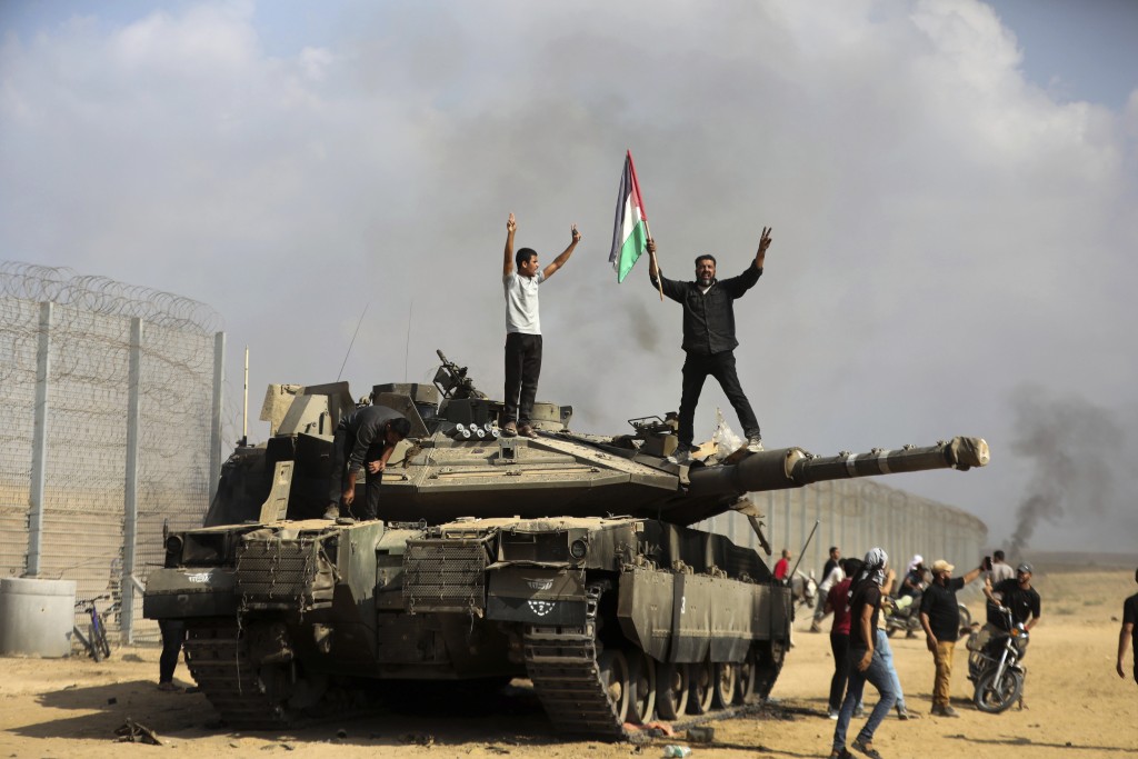 一輛以色列坦克在加沙南部被摧毀，巴人揮動旗幟慶祝。美聯社