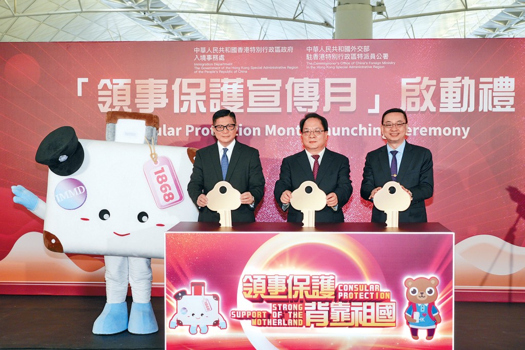 (左起)保安局局長鄧炳強、外交部駐港特派員公署副特派員潘雲東、入境處處長郭俊峯,與行李箱造型的「協助在外香港居民小組」吉祥物「阿邦」合照。