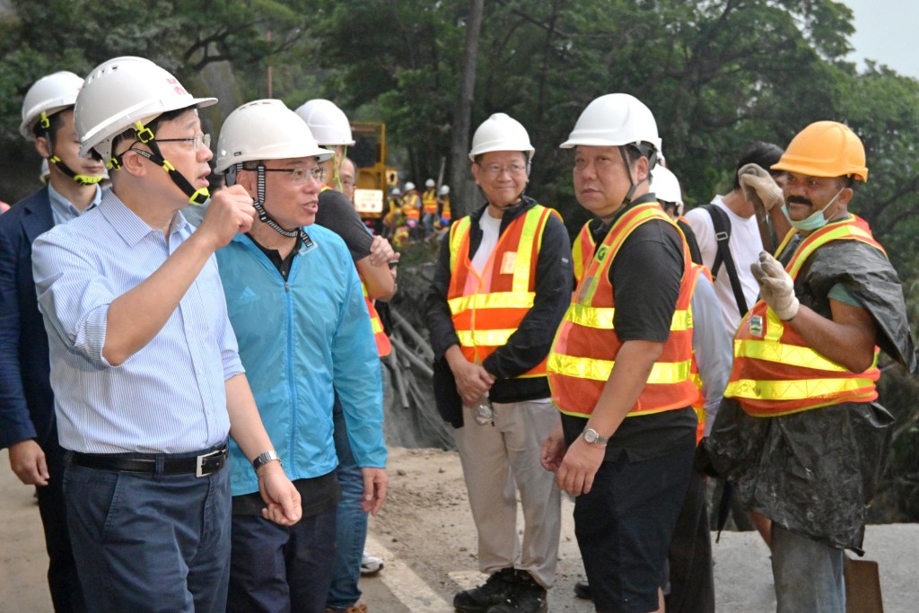 李家超（左一）和运流局局长林世雄（左二）为路面修复工程的工作人员打气。政府新闻处