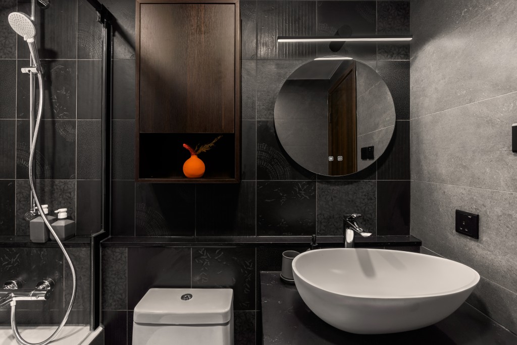 浴室打破傳統，主調是黑色，黑灰牆磚配黑框圓鏡，加上黑色洗手盆櫃，再配合白色浴室潔具