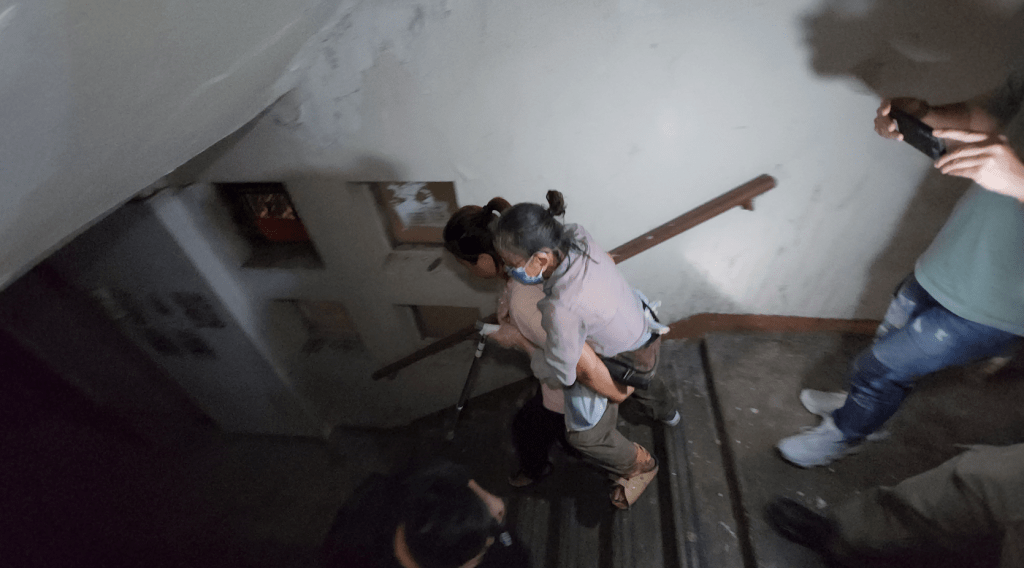 有老婦不便於行，有熱心居民背住她行十多層樓梯，汗流浹背。