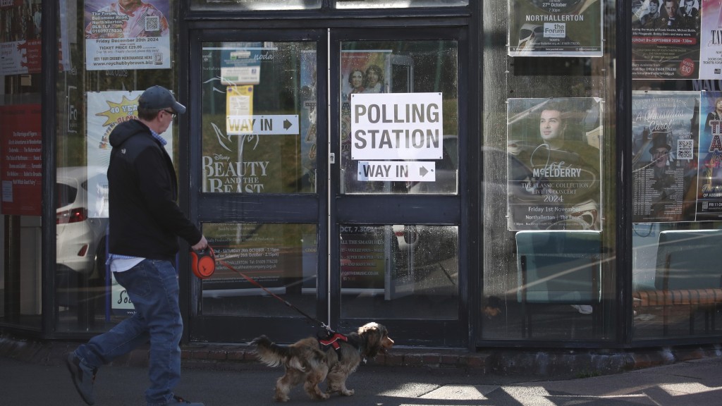 一名男子遛著狗经过英国北约克郡诺萨勒顿论坛剧院的投票站。  美联社