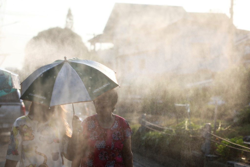 泰國持續高溫，兩名女子在路邊的灑水水霧中走過。路透社