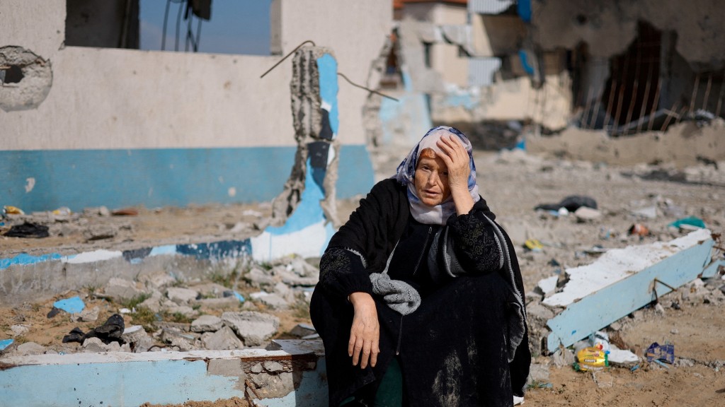 一名婦人坐在受損建築物旁的路𡒊休息。 路透社