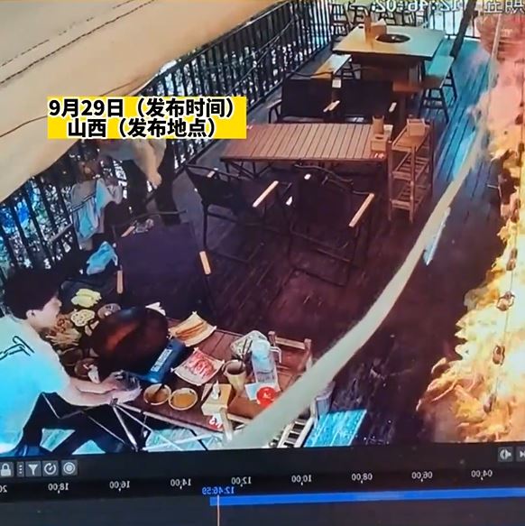 女食客突然起身点燃墙上的芒草装饰引发大火，叫同伴用水救火。影片截图