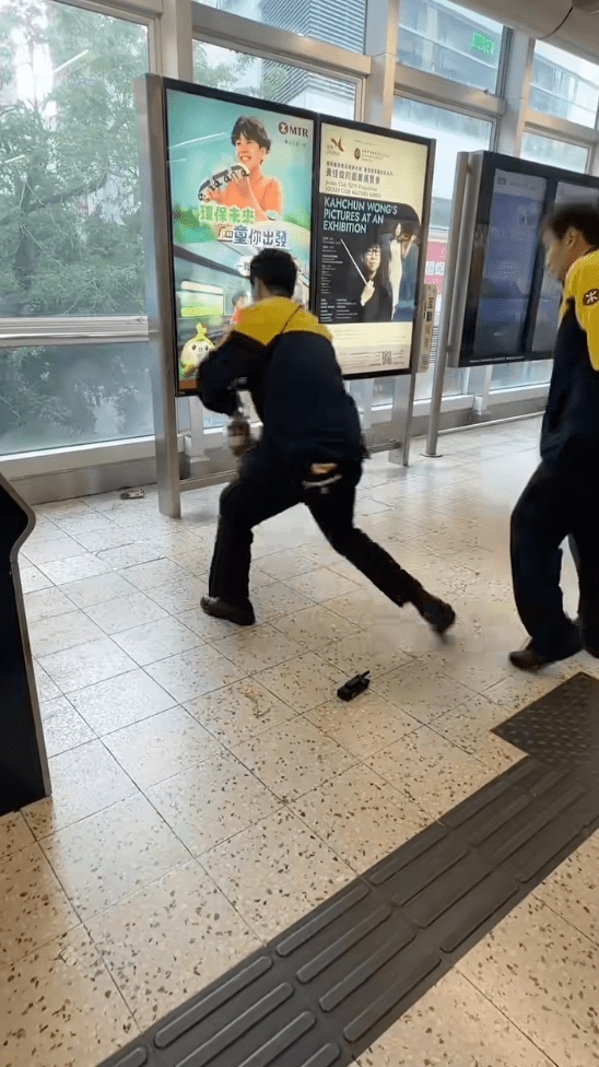 現場兩名男職員迅速採取行動，其中一人蹲下並拉出滅火筒的安全鎖針，另一名男同事則在旁協助。