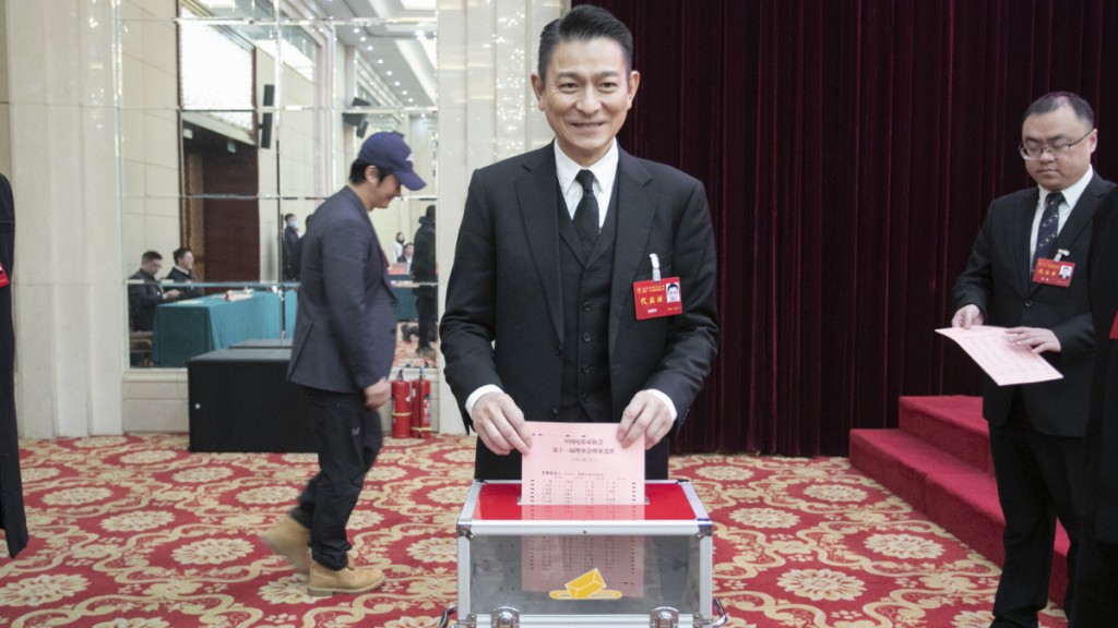 刘德华投票时脸露笑容，背后「路过」的戴帽男子，正是吴京。（《星岛》图片）