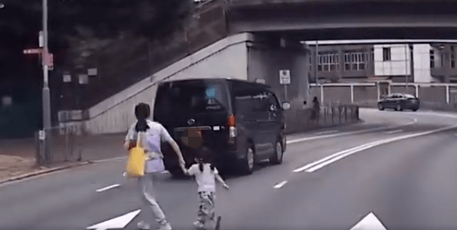 一名妇人胸前孭着幼婴，右手拖住女童，在界限街胡乱过路。车CAM截图