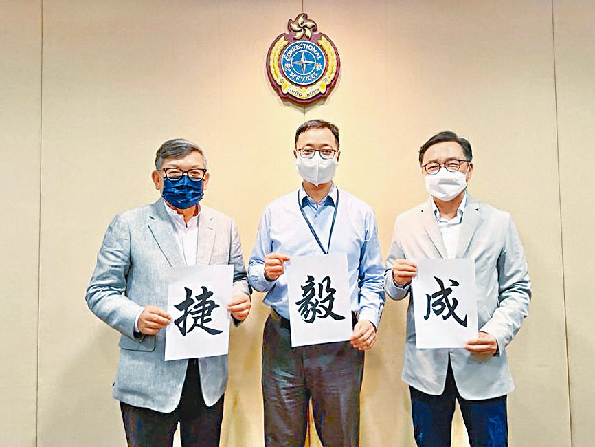 我以「成」字為同學打氣，本會嚴玉麟會長（左）送上一個「捷」字。中為懲教署黃國興署長。