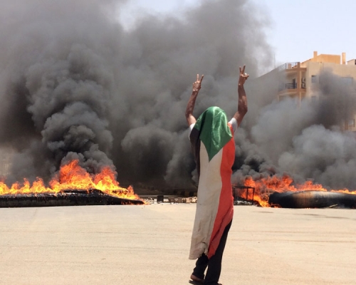 一名戴著蘇丹國旗的示威者在燃燒的輪胎和碎片前擺出勝利手勢。AP