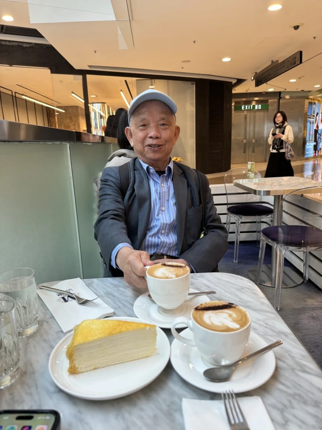 照片中鄔友正身穿白色圓領T恤及黑色羽絨外套,與助手一同坐在商場內的咖啡店品嚐咖啡及千層蛋糕,十分悠然自得。 照片中鄔友正身穿白色圓領T恤及黑色羽絨外套,與助手一同坐在商場內的咖啡店品嚐咖啡及千層蛋糕,十分悠然自得。