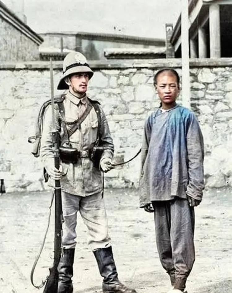 八國聯軍軍人抓著一名清人的辮子拍照（電腦補色）。