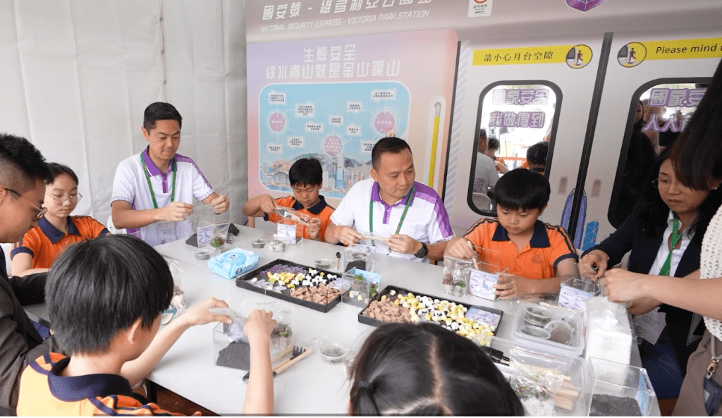 國安處處長江學禮及警務處助理處長(國家安全)郭嘉銓在國安處花卉展攤位內與小學生一同體驗製作生態箱。