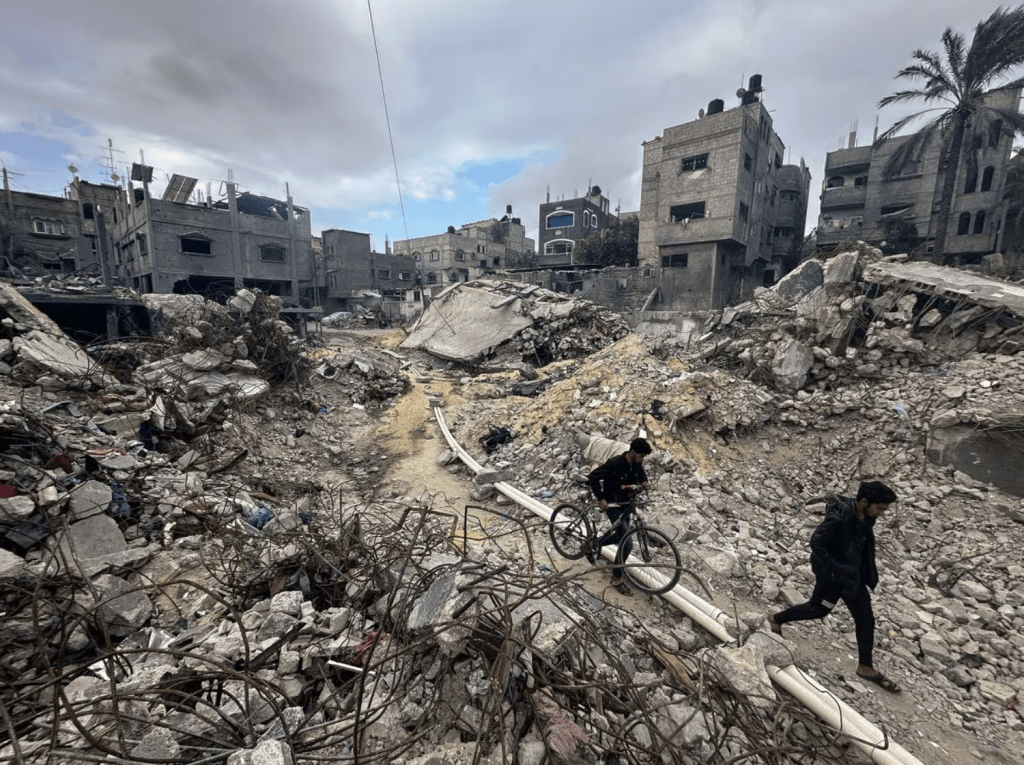 2023 年 11 月 27 日，在加沙走廊南部汗尤尼斯难民营，哈马斯和以色列暂时休战期间，巴勒斯坦人在瓦砾中行走，检查在冲突期间以色列袭击中被摧毁的房屋。路透社