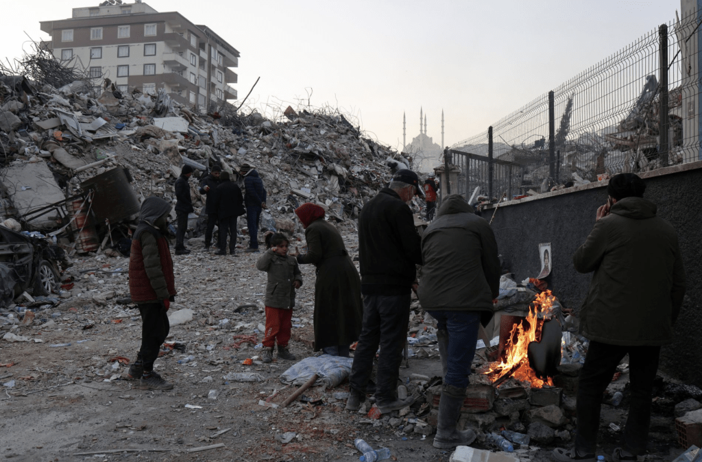 土耳其灾民站在被毁房屋废墟附近的火堆旁取暖。路透社
