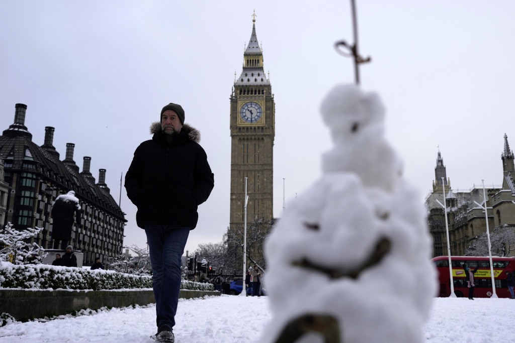 一名男子走过伦敦的一个雪人。冰雪席卷了英国的部分地区，寒冷的冬季条件将持续数天。AP