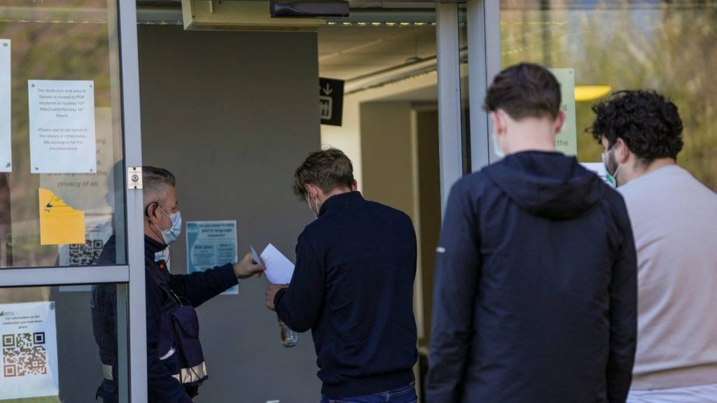 在英格蘭東南部一校園內，人們戴著口罩在臨時醫療中心排隊領取抗生素。（法新社）