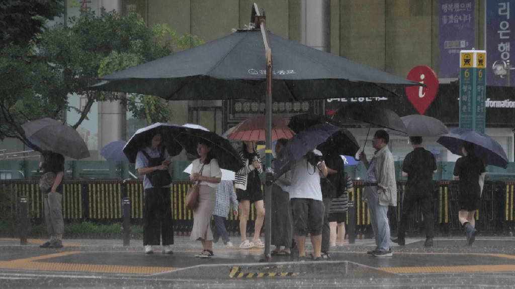 首爾民眾撐傘也濕透，有人躲在帳篷下等過馬路。 （美聯社）