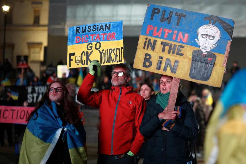 在伦敦，民众披著乌克兰国旗并高举标语，其中一个写著将普京丢入垃圾桶。路透社