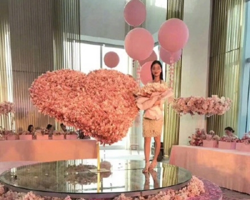 女子站在人民幣組成的巨大的心型「有錢花」旁。(網圖)