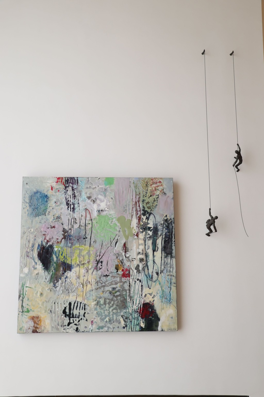加拿大画家Su Sheedy的抽象画作旁边，挂了两个向上爬的公仔，寓意永远向前。